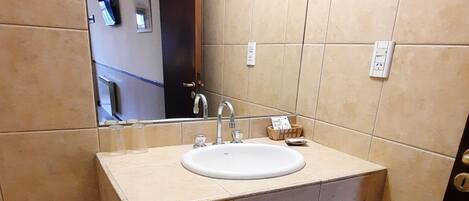 A bathroom with a sink, mirror, and towel rack. There is a toilet and a shelf with towels.