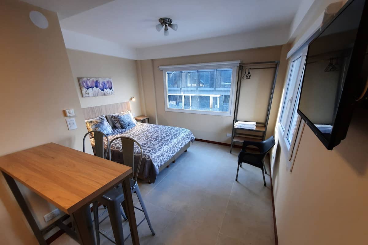 Een slaapkamer met een bed, een bureau en een stoel. Er is een raam met uitzicht op een gebouw.