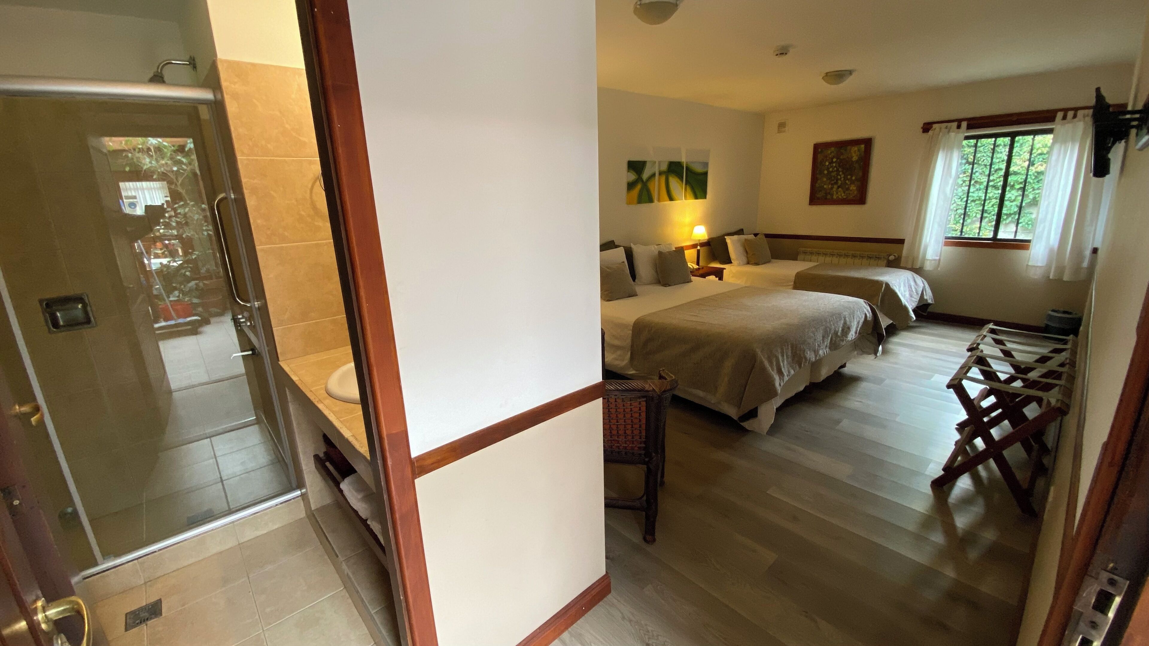 A hotel room with a shower, two beds, a window with curtains, and a painting on the wall.