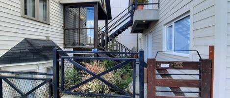 Un immeuble résidentiel doté d’un portail en métal noir, d’un escalier en bois et d’un balcon agrémenté d’un pot de fleurs.