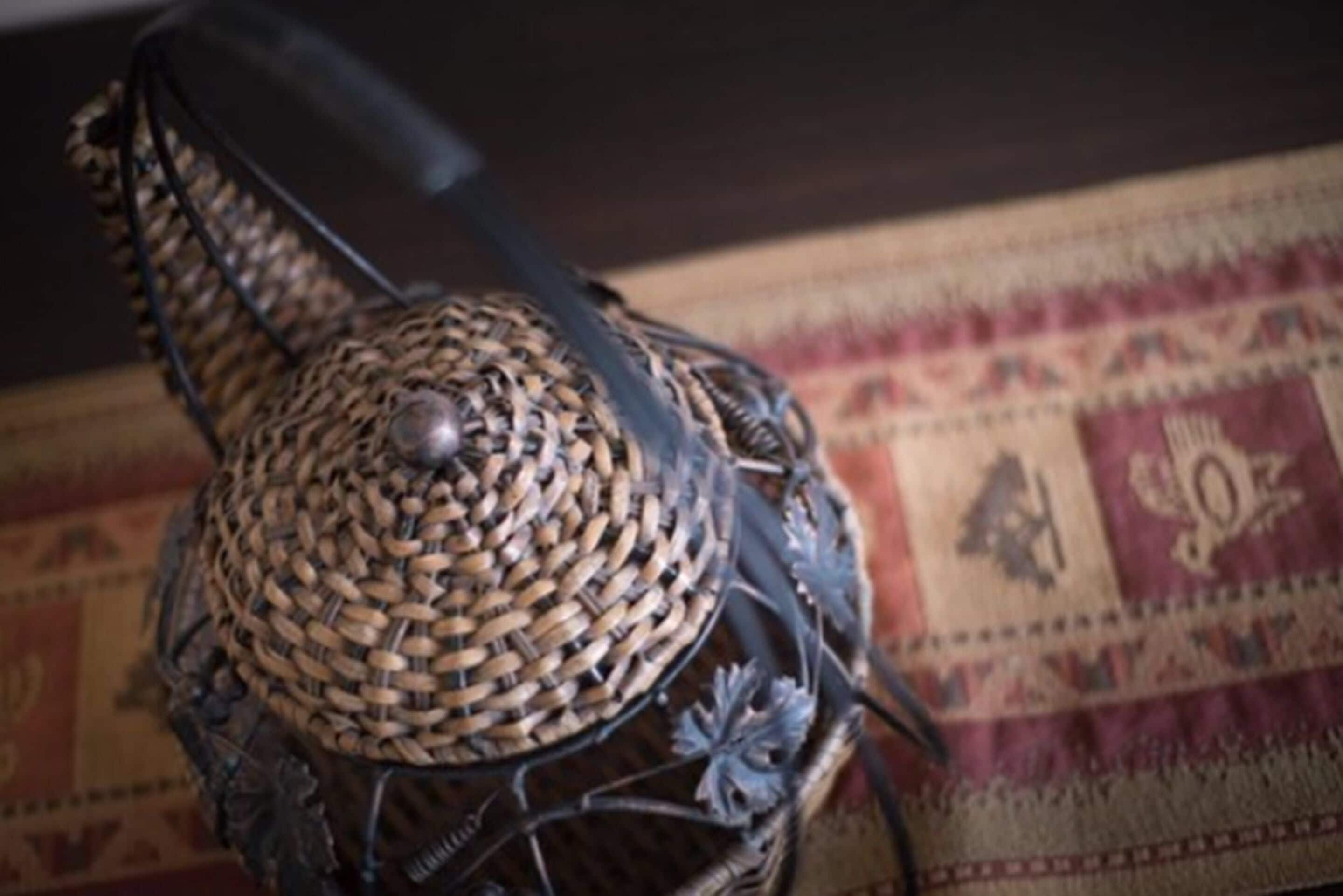 A woven basket with a metal handle and decorative elements, placed on a patterned fabric.