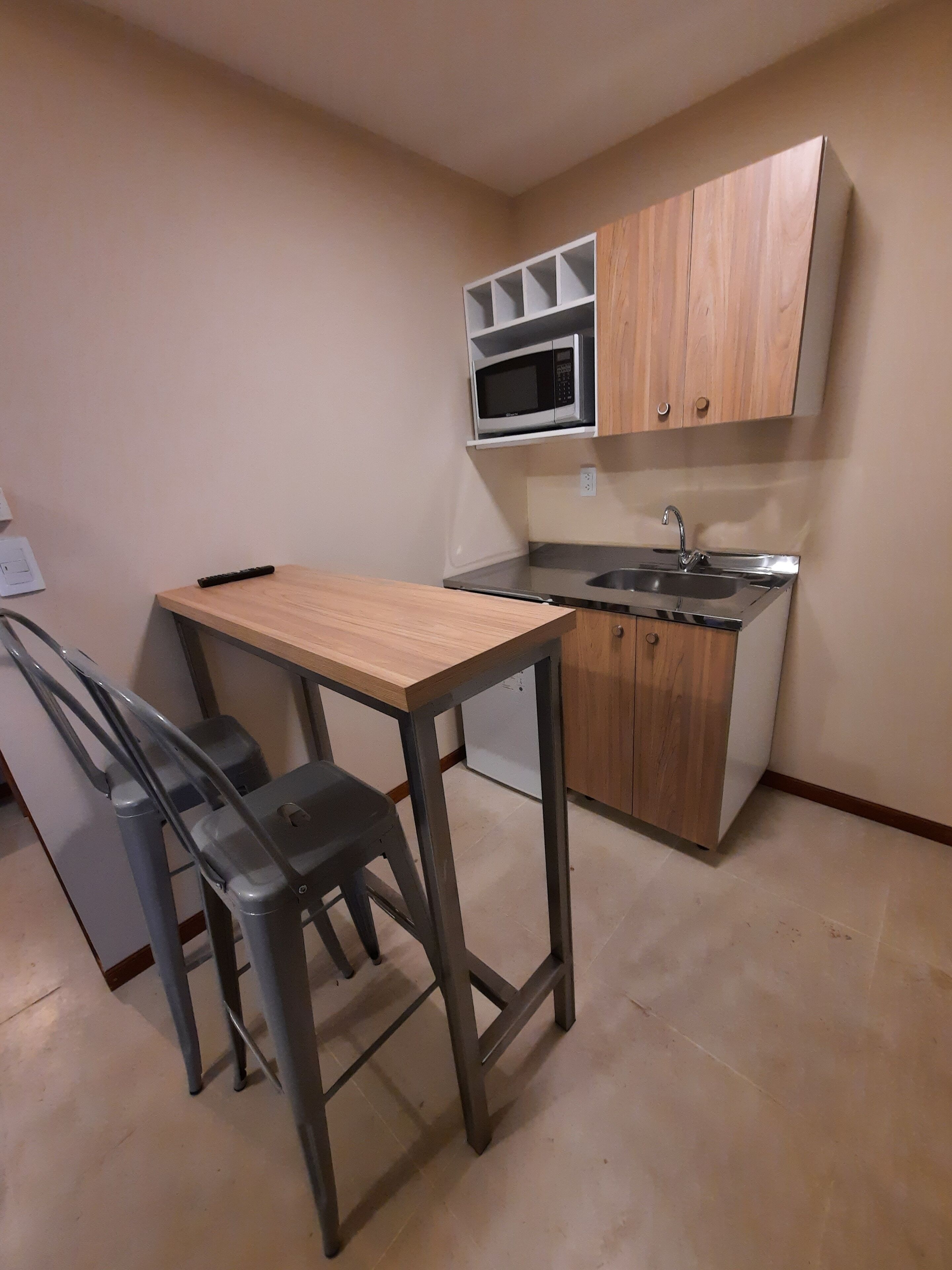 Una cocina compacta con una mesa de madera y dos sillas, un microondas y un lavabo.