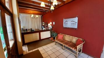 Et receptionsområde med en træreception, rød væg, et skilt der siger "HOTEL STRAL" og en fletsofa med rød pude.