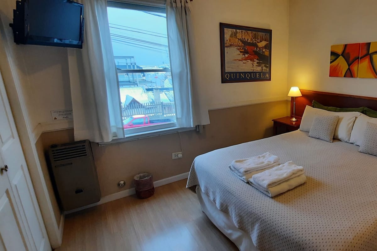 Een hotelkamer met een groot bed, twee nachtkastjes met lampen, een raam met gordijnen, een tv aan de muur en een schilderij.