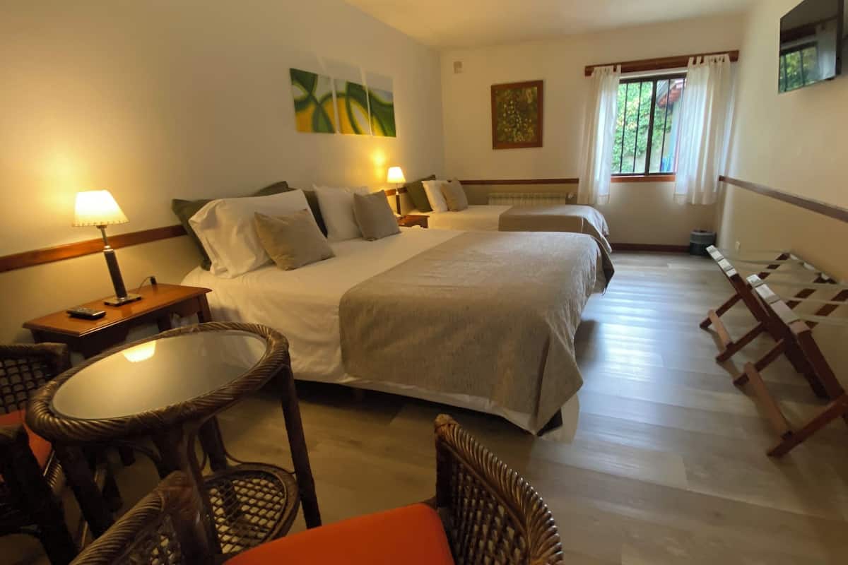 Een hotelkamer met twee bedden, een zithoek met een stoel en een tafel, een klein raam met gordijnen, en kunstwerken aan de muren.