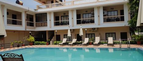 A hotel with a pool area, multiple balconies, and lounge chairs.