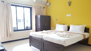 A bedroom with a bed, a wardrobe, a window with curtains, an air conditioning unit, and a bedside table.