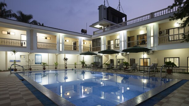 A swimming pool with lounge chairs and umbrellas, surrounded by a building with multiple balconies and a checkered floor.