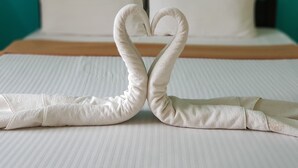 A bed with a white pillow and a towel arranged in a heart shape.