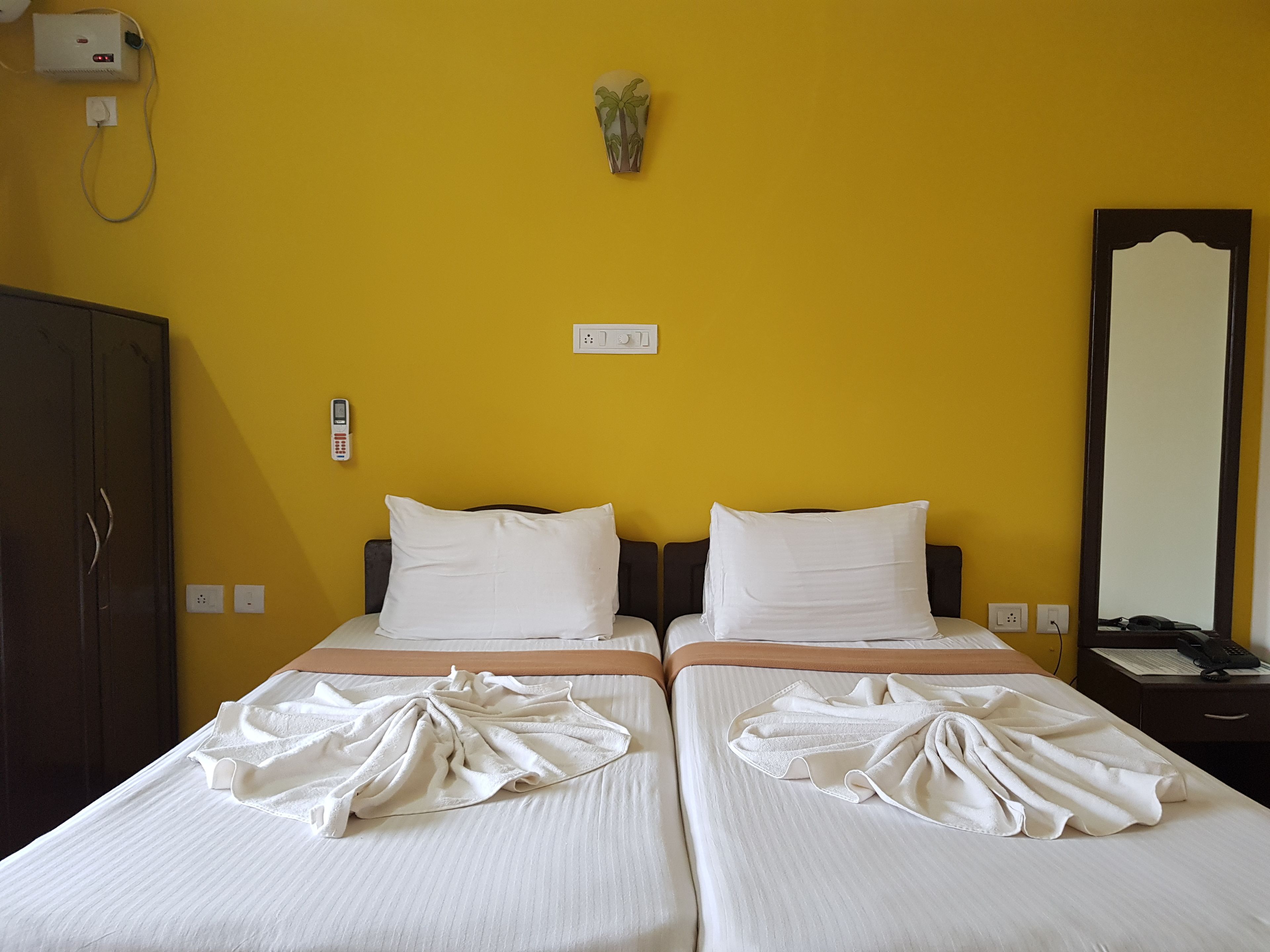 A hotel room with two beds, a wardrobe, a telephone, and a mirror.