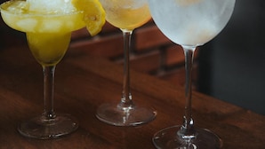 Three glasses of iced drinks on a wooden table with a brick wall background. - The Bricks Hotel (Dumaguete)