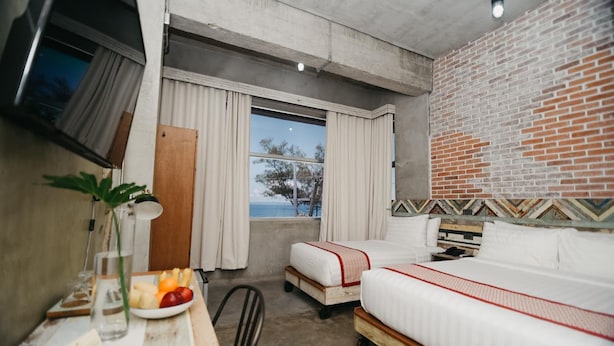 A hotel room with a bed, a desk with a plant and fruit, a TV, and a window with a view. - The Bricks Hotel (Dumaguete)