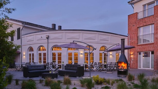A building with a curved facade, outdoor seating area with tables and chairs, and a wood-burning stove.