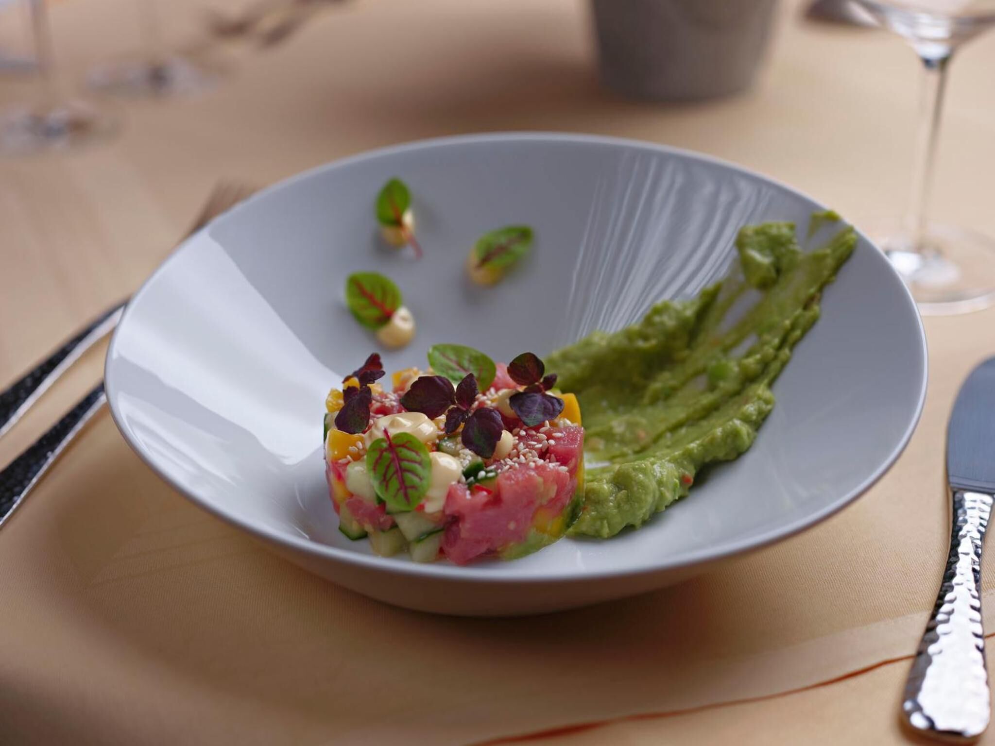 Prato com carne picada, legumes e guarnições, acompanhado por uma fatia de abacate sobre um prato branco.