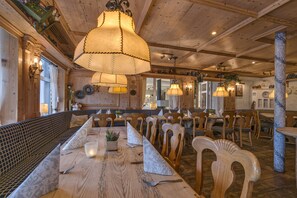 A restaurant with wooden furniture, hanging lamps, and a long communal table. - Hotel Burg-Klause (Fehmarn)