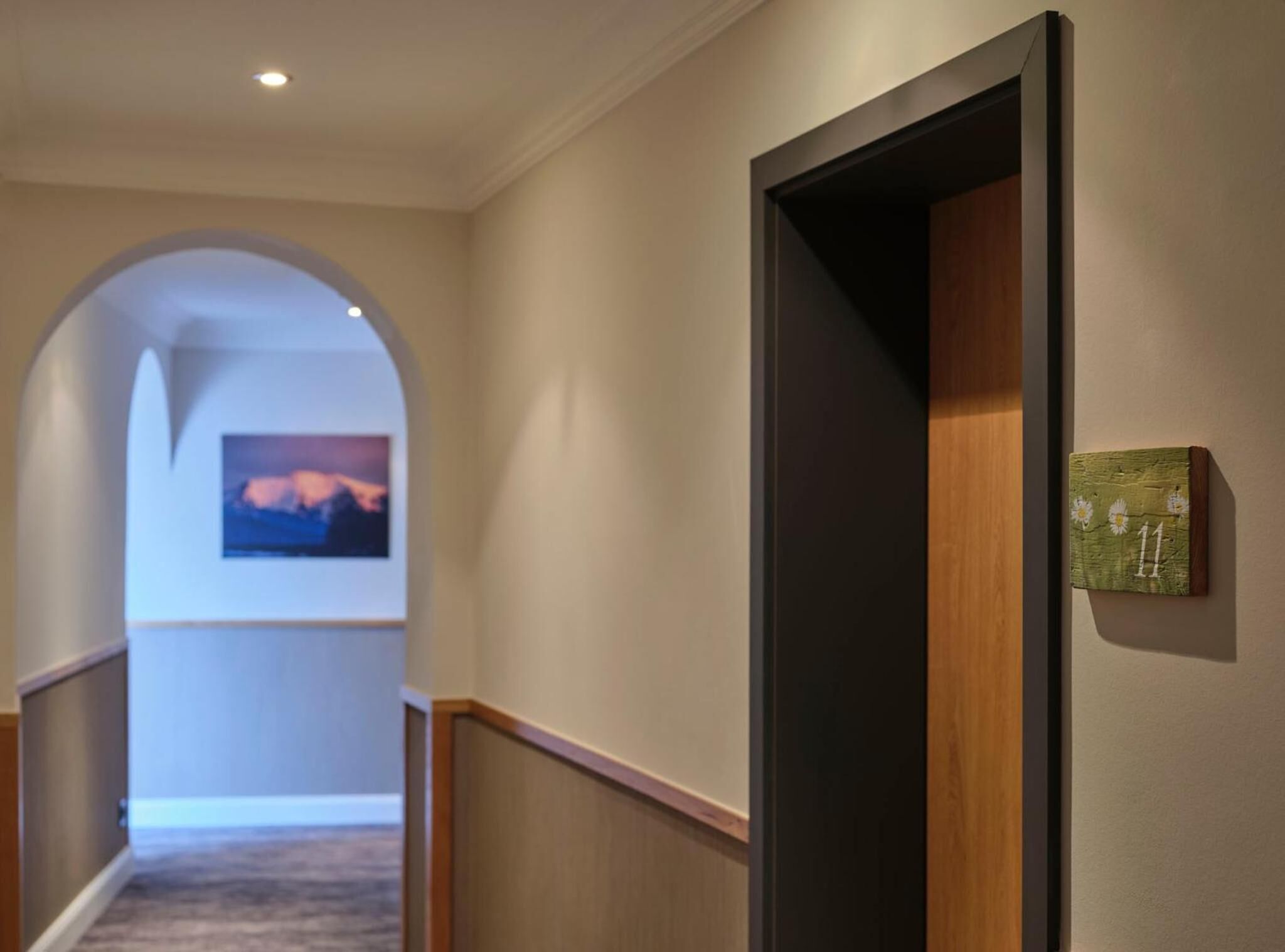 A hallway with a wooden door, a number plaque, and a painting on the wall.