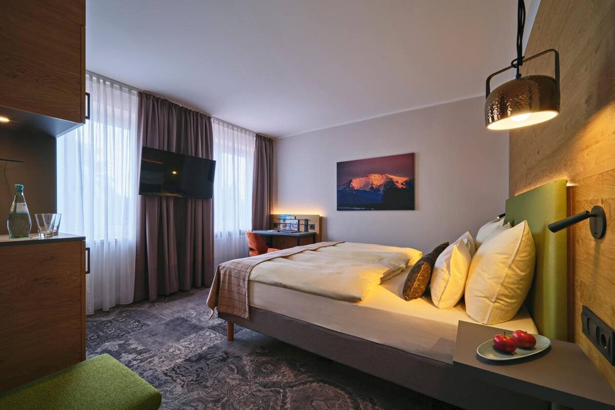 Ein Hotelzimmer mit Bett, Schreibtisch mit Fernseher, einem Gemälde an der Wand und Bergblick.