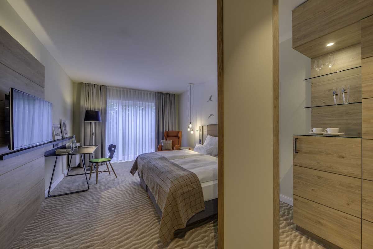 Ein modernes Hotelzimmer mit einem großen Bett, einem Schreibtisch mit Stuhl, einem Flachbildfernseher und einer Minibar.