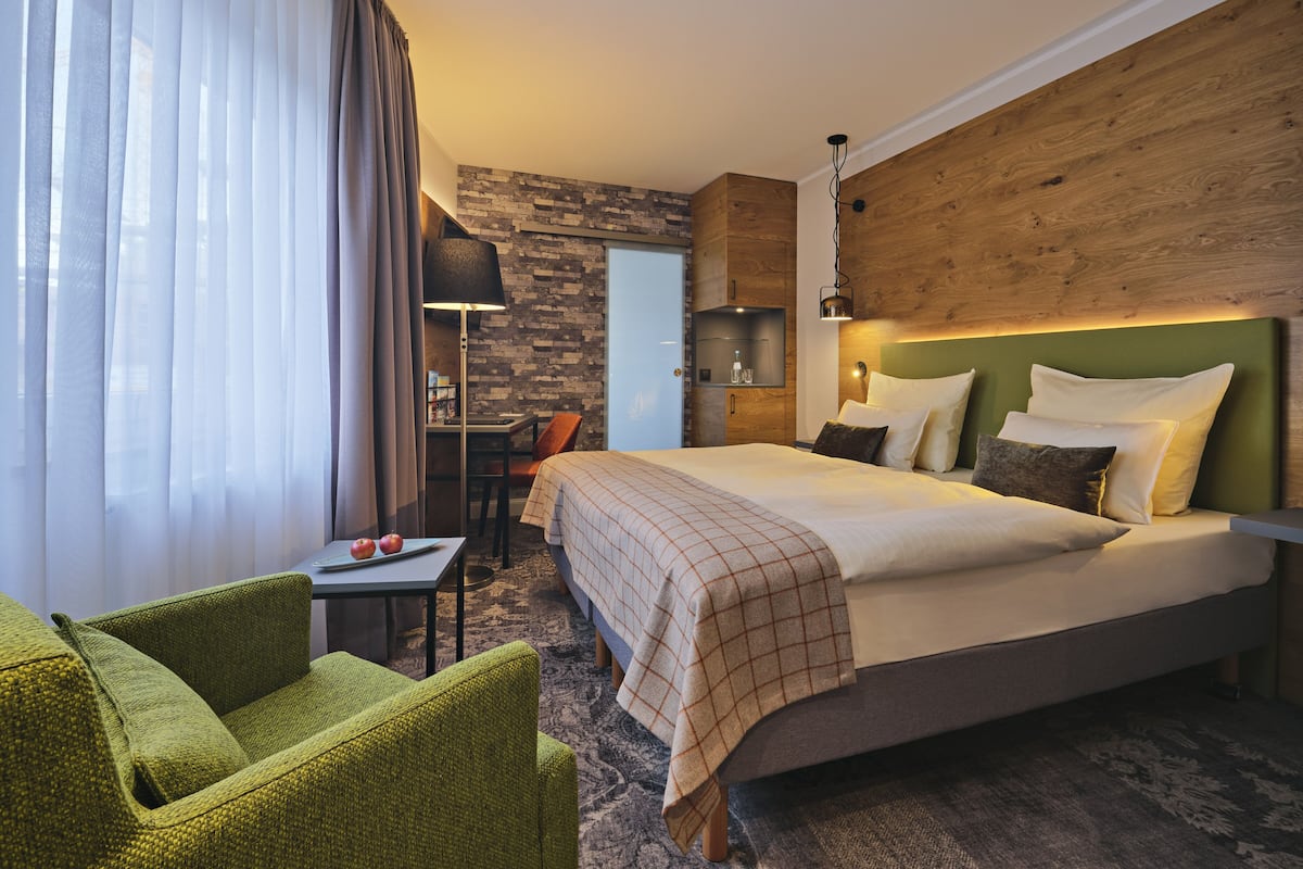 Ein Hotelzimmer mit einem großen Bett, einem Schreibtisch und einem grünen Sessel.