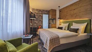 A hotel room with a large bed, a desk, and a green armchair.