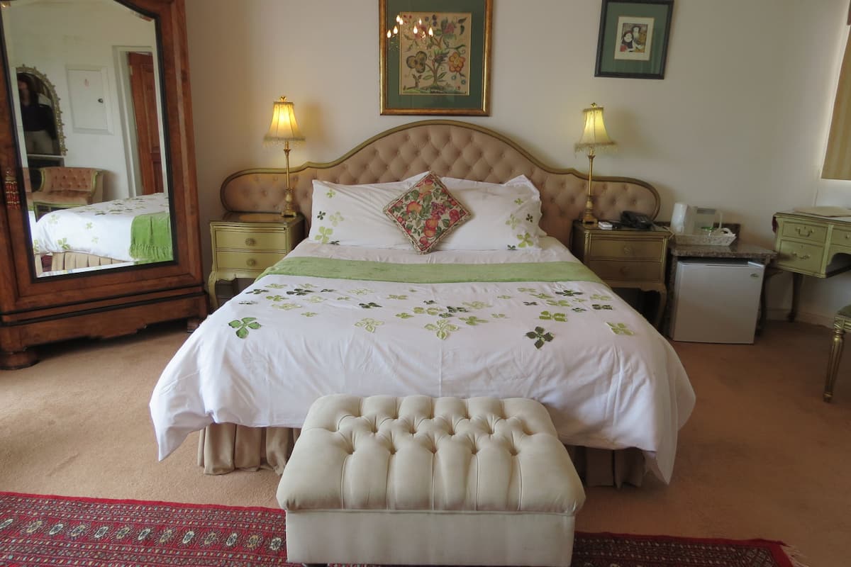 A neatly arranged bedroom with a large bed, two bedside tables, a small refrigerator, and a mirror.