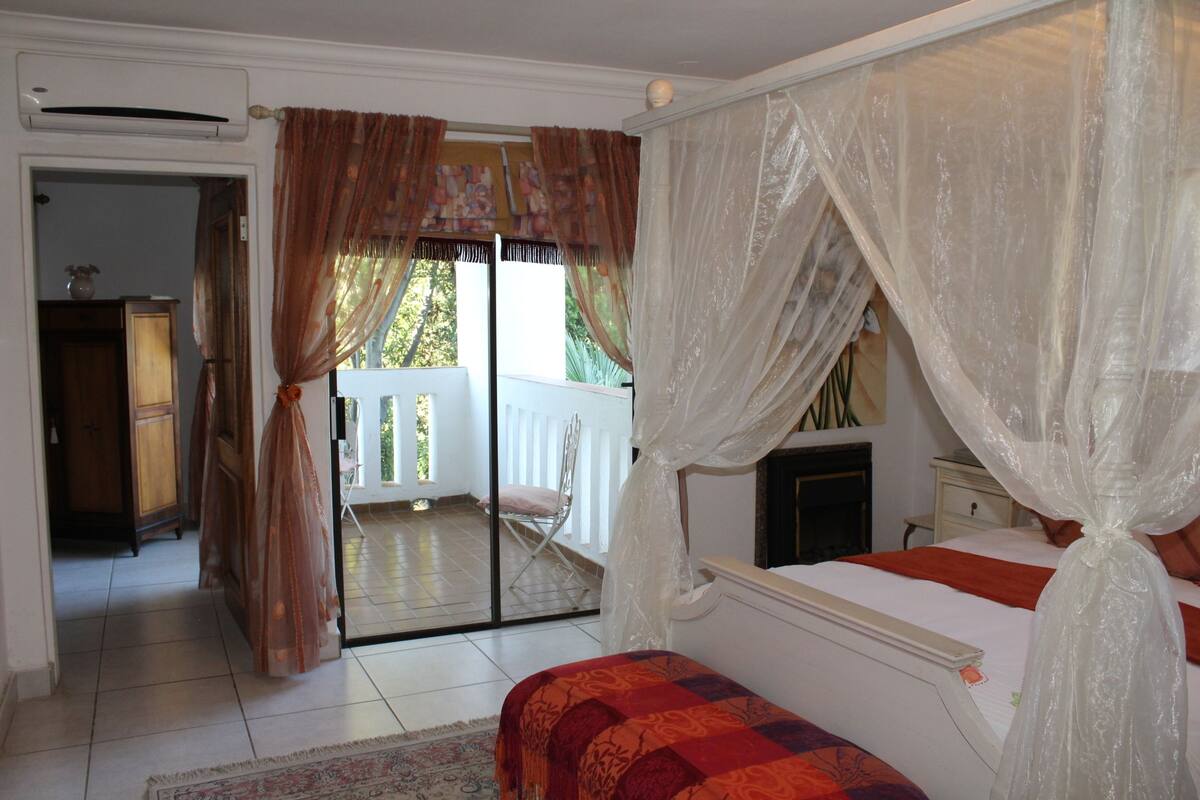 A bedroom with a bed, a nightstand, a window with curtains, and a view of the outside balcony.