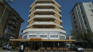 A multi-story hotel with a yellow and white facade, outdoor seating area, and a sign reading "Hotel FABIUS". - Hotel Fabius (Bellaria-Igea Marina)