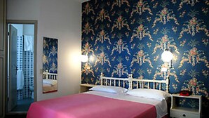 A bedroom with a bed, two bedside tables, a nightstand, a mirror, and a floral wallpaper. - Hotel Fabius (Bellaria-Igea Marina)