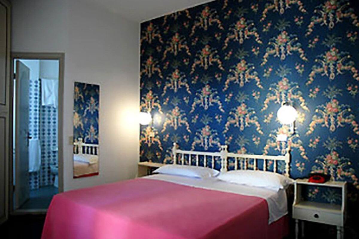 A bedroom with a bed, two bedside tables, a nightstand, a mirror, and a floral wallpaper.