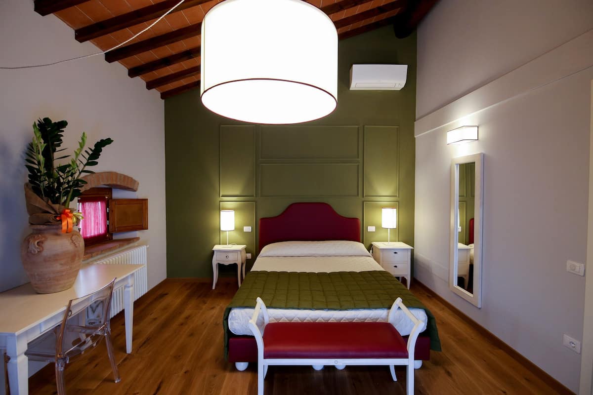 Un dormitorio con techo de madera, una cama con cabecera roja, lámparas de noche, un espejo y un escritorio con silla.