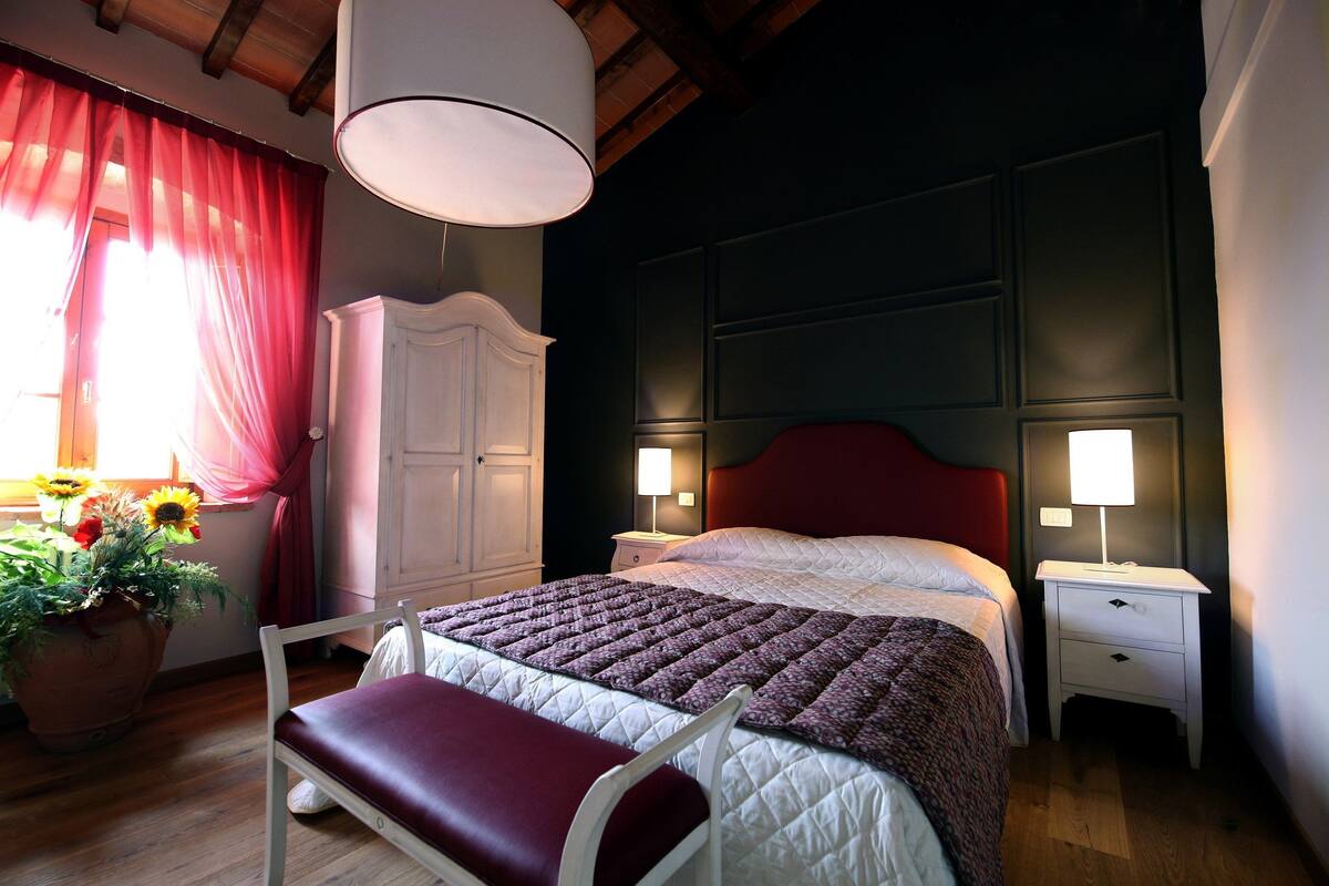 Un dormitorio con cama, mesitas de noche, un armario y una ventana con cortinas.