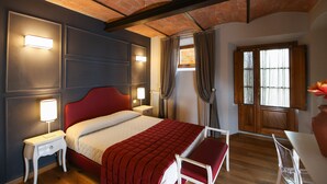 A hotel room with a red bed, white nightstand, and a small table with a chair. There is a window with curtains and a view of the outside.