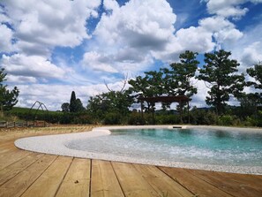 A wooden deck surrounding a swimming pool with a pergola and trees in the background. - Agriturismo Casanova (Scandicci)