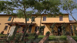A yellow building with a tiled roof, a stone staircase, and a garden with flowers and plants.