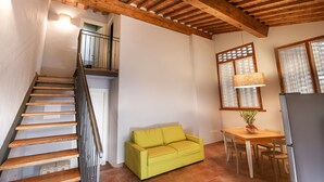 A staircase with wooden steps and a metal railing, a yellow sofa, a dining table with chairs, and a window with curtains.