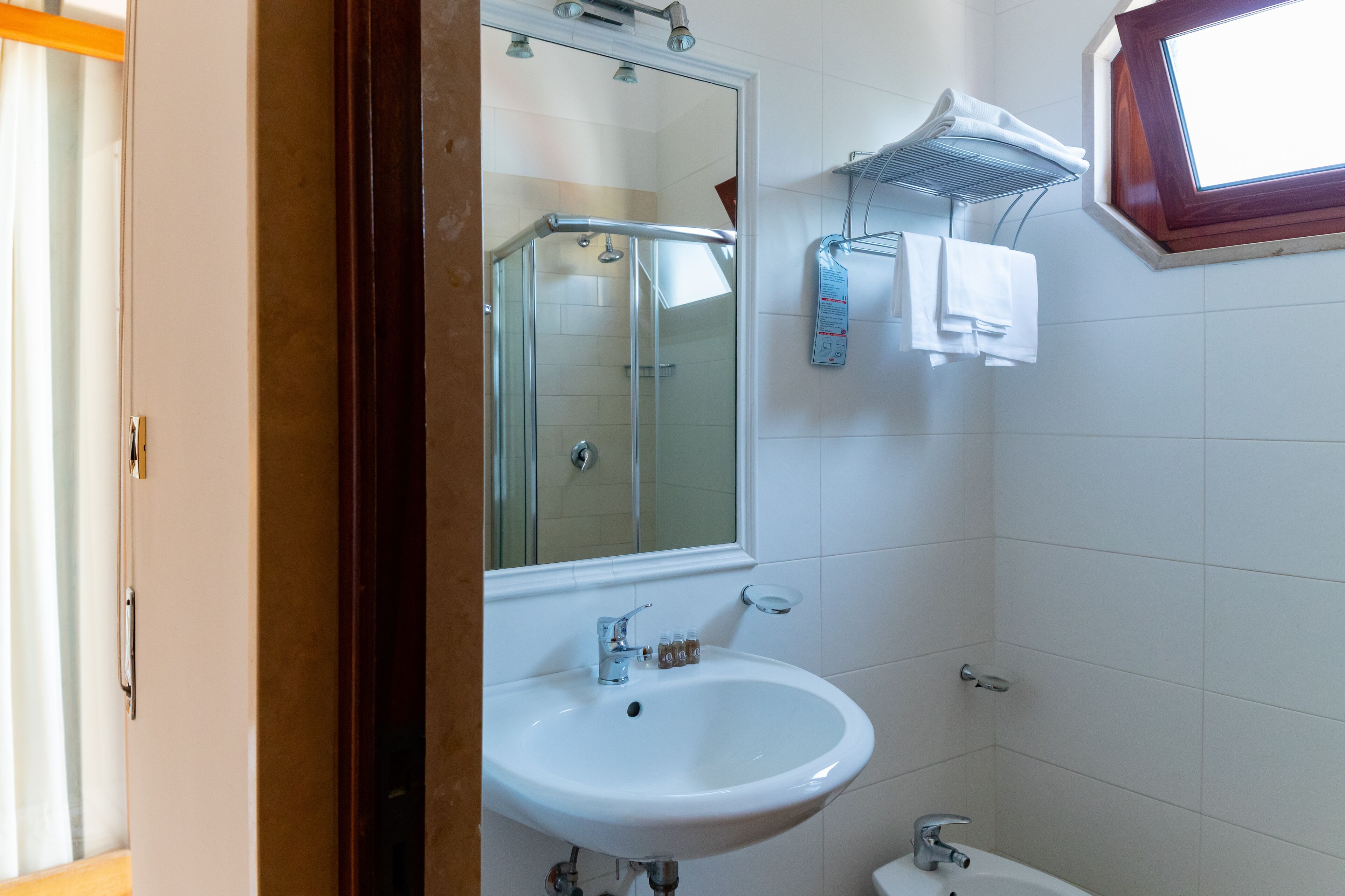 Un baño con cabina de ducha de vidrio, un lavabo blanco y un ventanal sobre el lavabo.