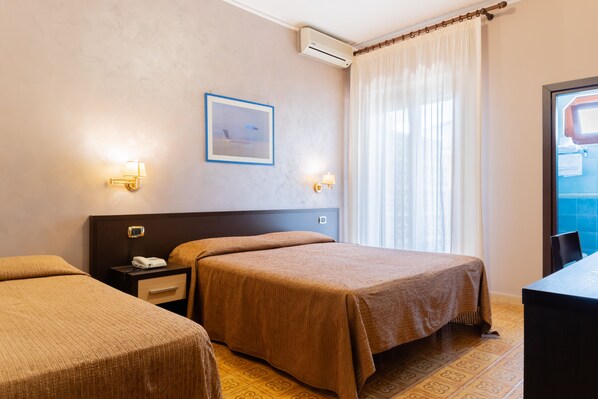Quarto de hotel com duas camas de solteiro, mesa de cabeceira com telefone, luminárias de parede, quadro decorativo e janela com cortinas.