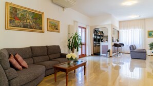Un salon avec un canapé, une table basse et une plante en pot. Il y a un tableau au mur et une porte qui donne sur une autre pièce.