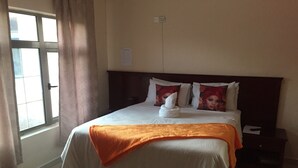 A hotel room with a bed, a nightstand, a window with curtains, and a wall socket. - Warm Hands Hotel (Kanye)