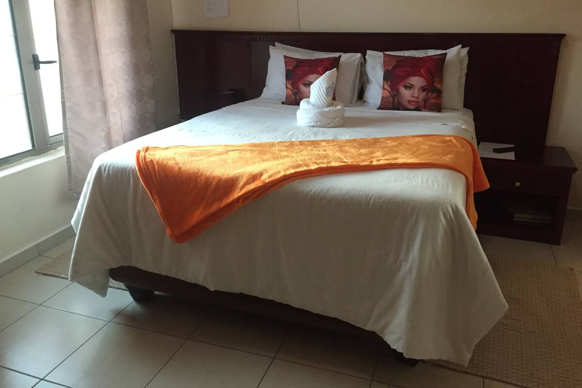 Una cama bien hecha con una colcha blanca y naranja, dos almohadas con un diseño floral y un cabecero de madera.