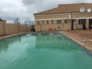 A swimming pool with a tiled deck, a lifebuoy, and a building with satellite dishes in the background. - Warm Hands Hotel (Kanye)