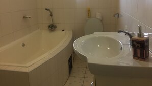 A bathroom with a bathtub, sink, toilet, and a window providing natural light. - Warm Hands Hotel (Kanye)