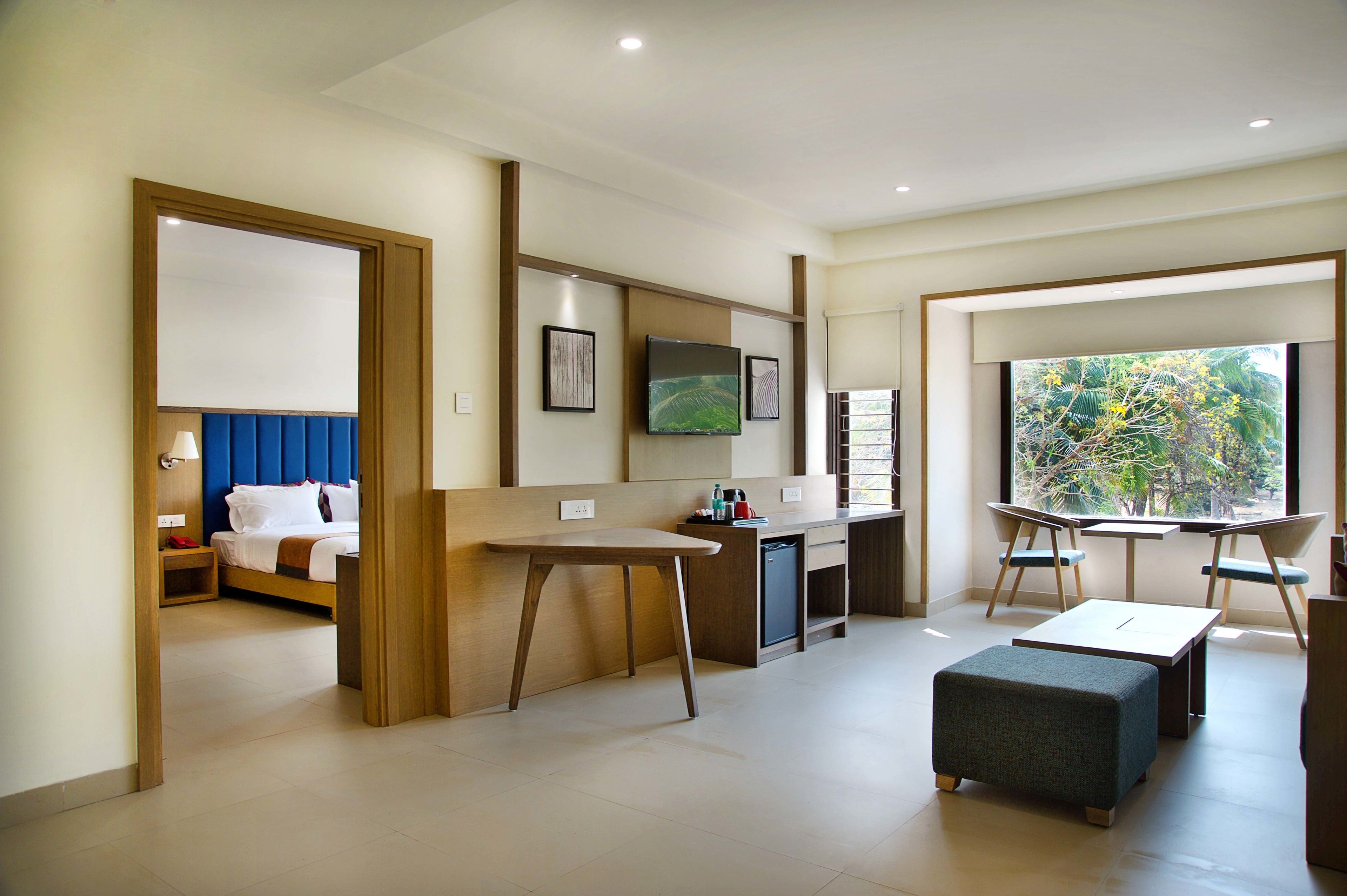 A modern hotel room with a bed, a desk, a chair, and a view of the outdoors.