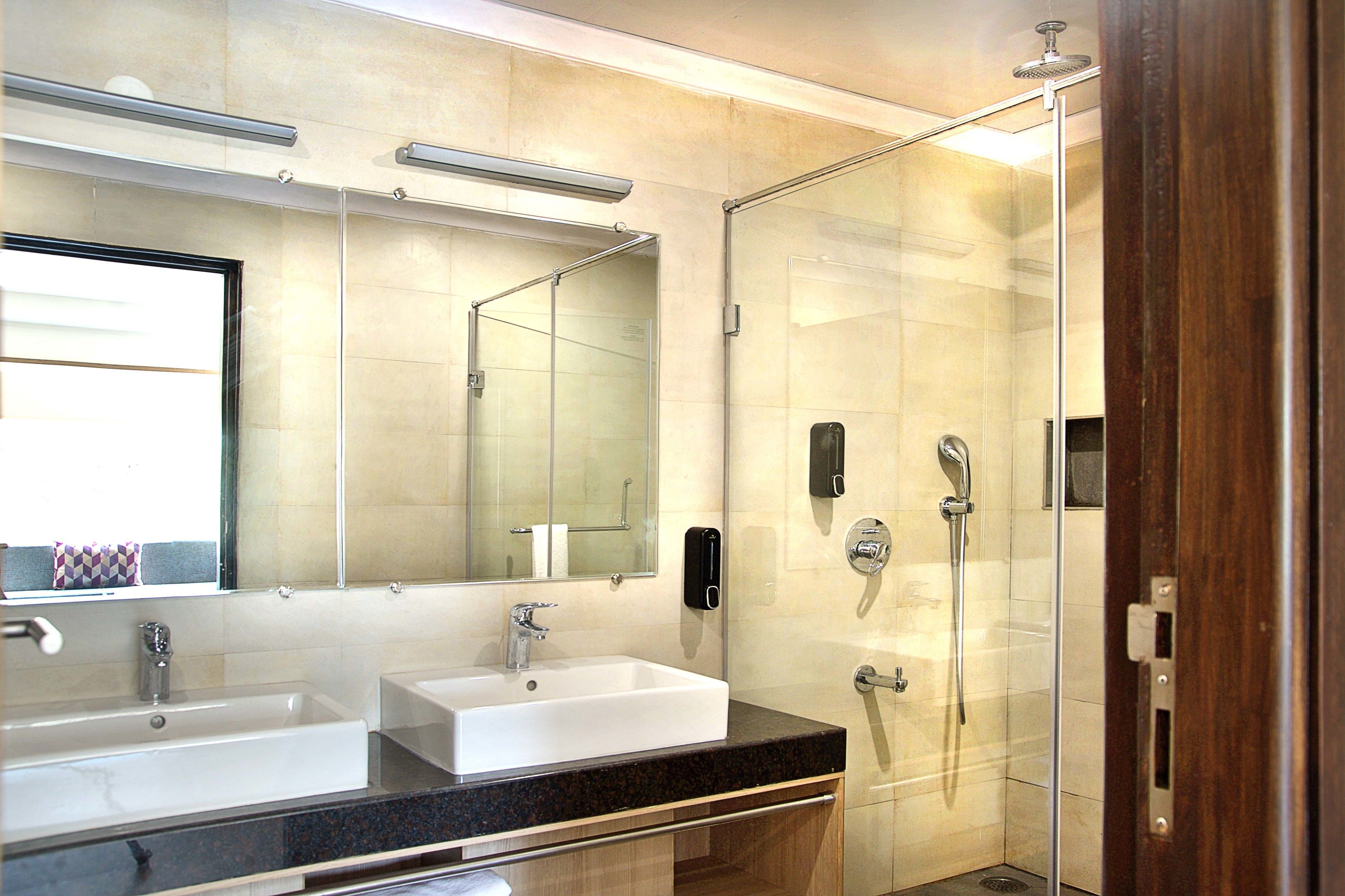 A modern bathroom with two sinks, a large mirror, and a glass-enclosed shower area.