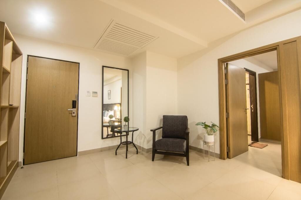 A room with a wooden door, a mirror, a small table, a chair, and a potted plant.