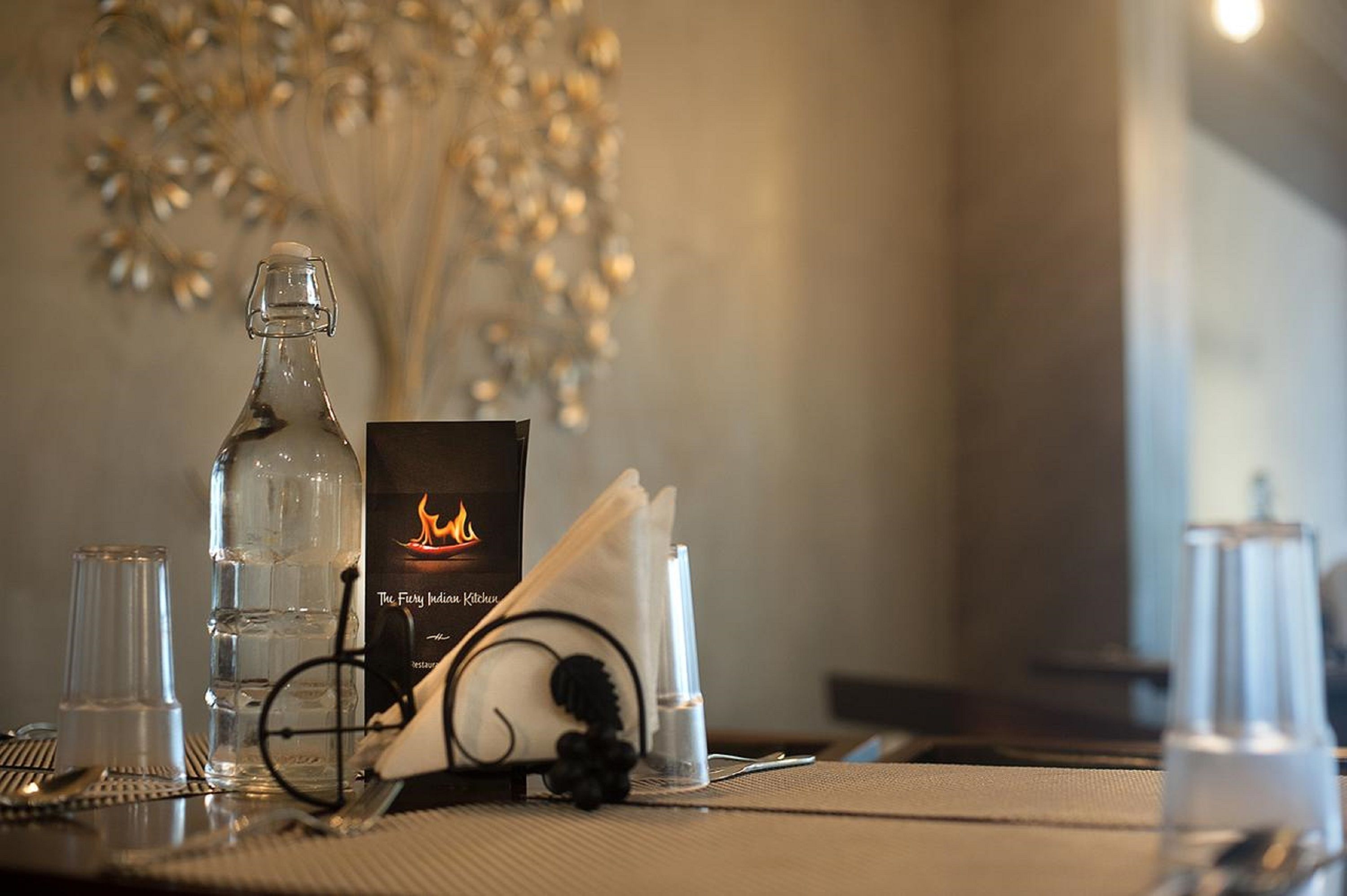 A table set with a bottle, glasses, a menu, and a decorative wall.