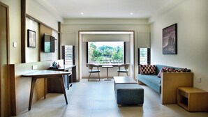 A modern living room with a sofa, a coffee table, a TV, and a dining area with chairs and a table. - Purple Cloud Hotel (Bengaluru)