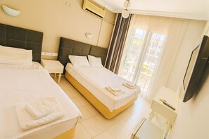 A hotel room with two beds, a nightstand, a TV, and a window with curtains. - Karadede Hotel (Cesme)