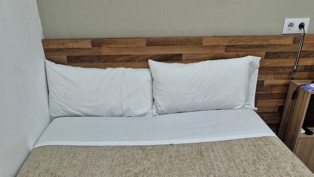 A neatly made bed with white linens, a wooden headboard, and a beige textured bedspread. Two folded towels with toiletries are placed on the bed. - Hostal Elkano (Barcelona)
