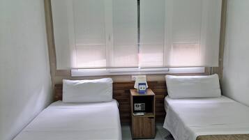 Habitación de hotel con dos camas individuales, una mesita de noche de madera con radio y una ventana con persianas.